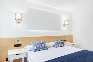 A modern hotel room with a wooden headboard, two bedside tables, a large bed with white bedding and blue patterned pillows, and wall-mounted light fixtures. - Hotel THB Los Molinos - Adults Only (Ibiza Town)