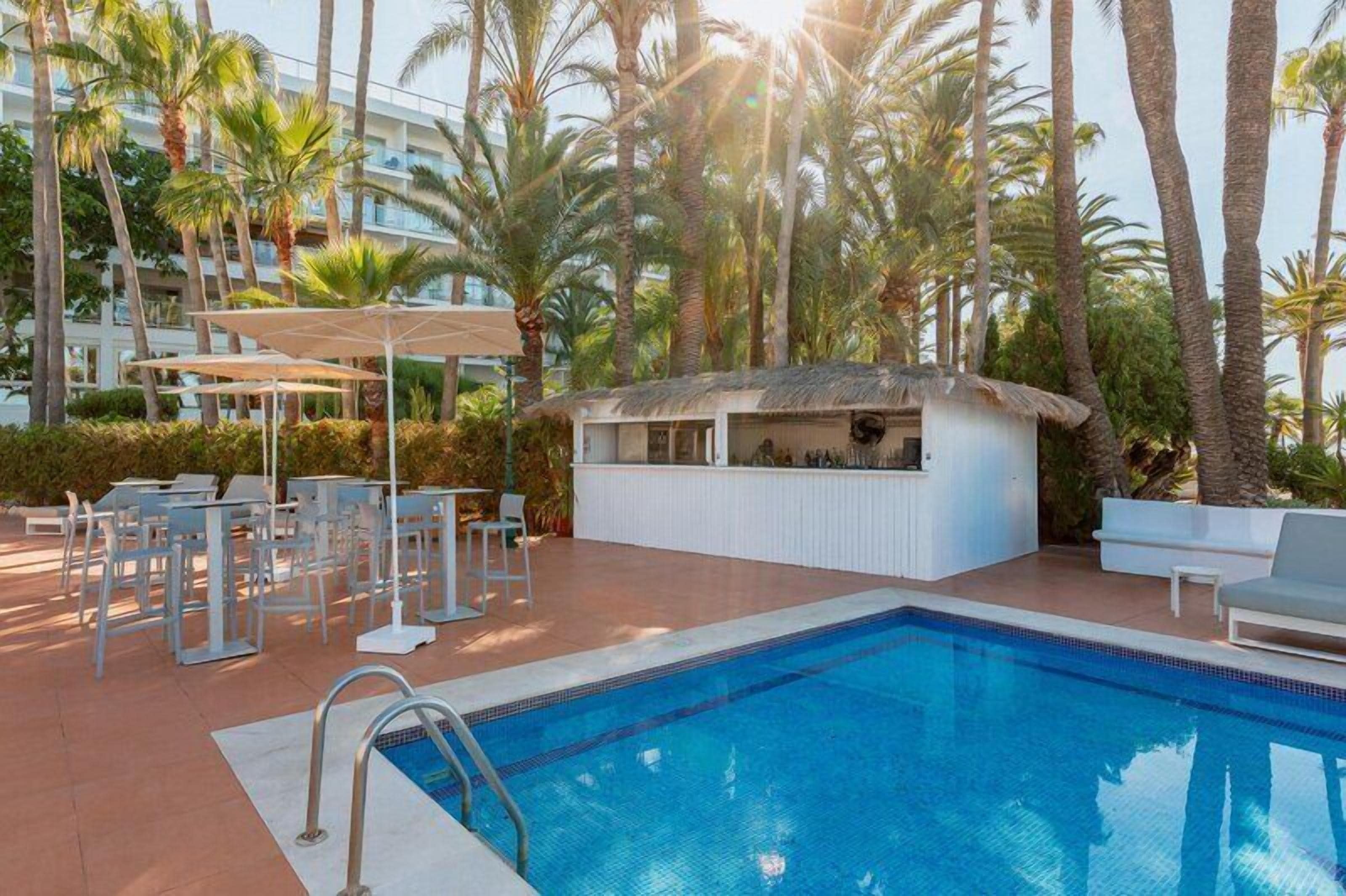 Un área de piscina con sillones de descanso, un bar y palmeras.