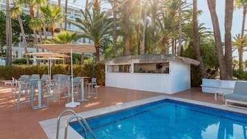 Un área de piscina con sillones de descanso, un bar y palmeras.