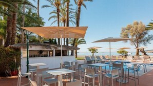 Zona de piscina al aire libre con sillones de playa y sombrillas, un bar y vistas a la playa.