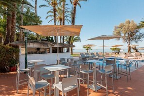 An outdoor pool area with lounge chairs and umbrellas, a bar, and a view of the beach. - Hotel THB Los Molinos - Adults Only (Ibiza Town)