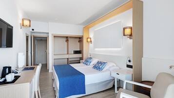 Habitación de hotel moderna con cama, escritorio y silla, una mesita con lámpara y televisor montado en la pared.