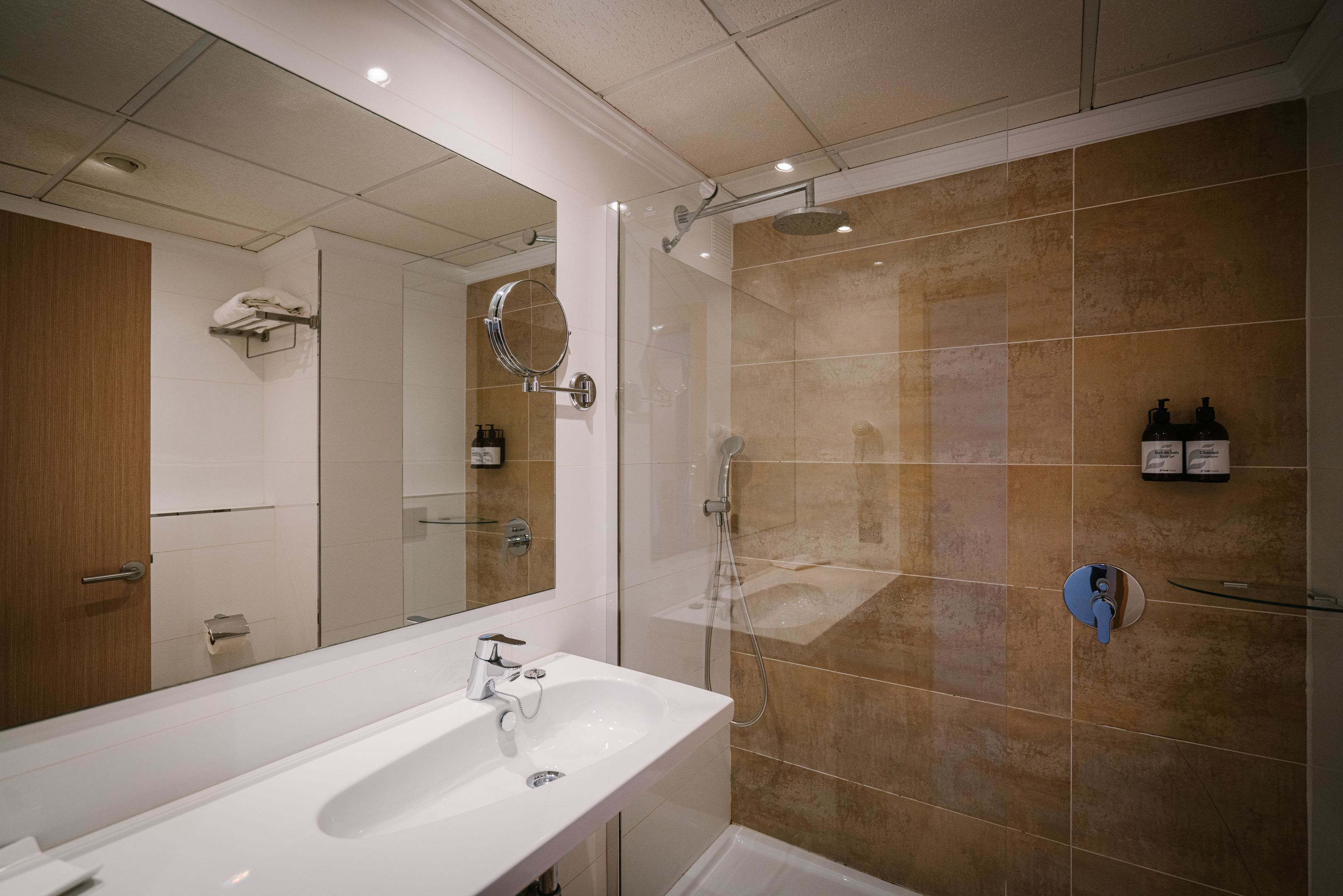 A modern bathroom with a large mirror, a white sink, and a glass-enclosed shower area.