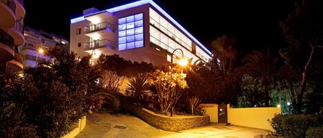 Un edificio moderno con una entrada bien iluminada, un muro de contención de piedra y un camino pavimentado que conduce a la entrada.