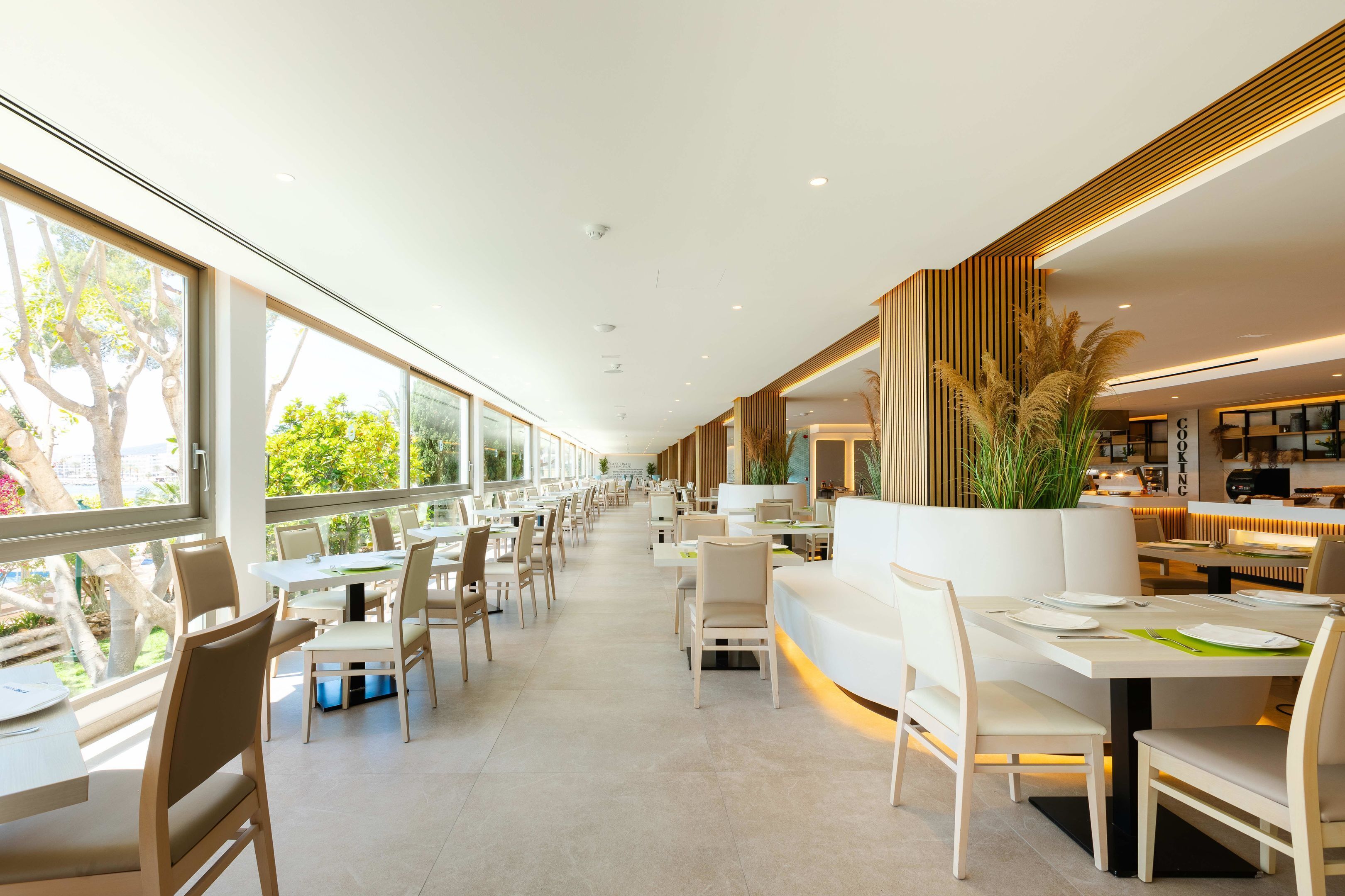 Un restaurante moderno con mesas y sillas largas, ventanas amplias y un interior limpio y minimalista.