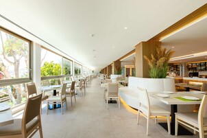 Um restaurante moderno com mesas e cadeiras compridas, janelas amplas e um interior limpo e minimalista.