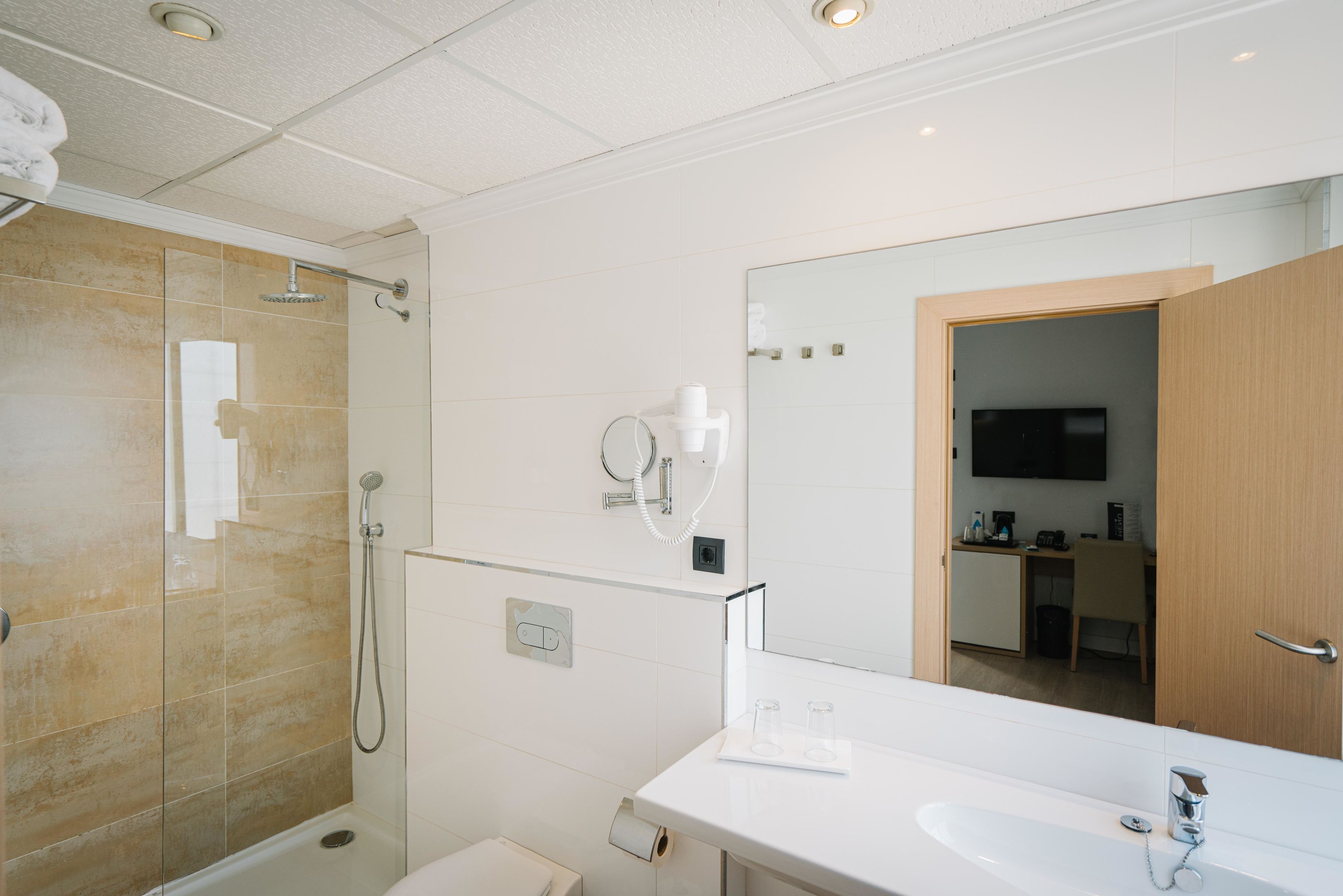 Un baño moderno con ducha de vidrio, lavamanos blanco y un espejo grande.