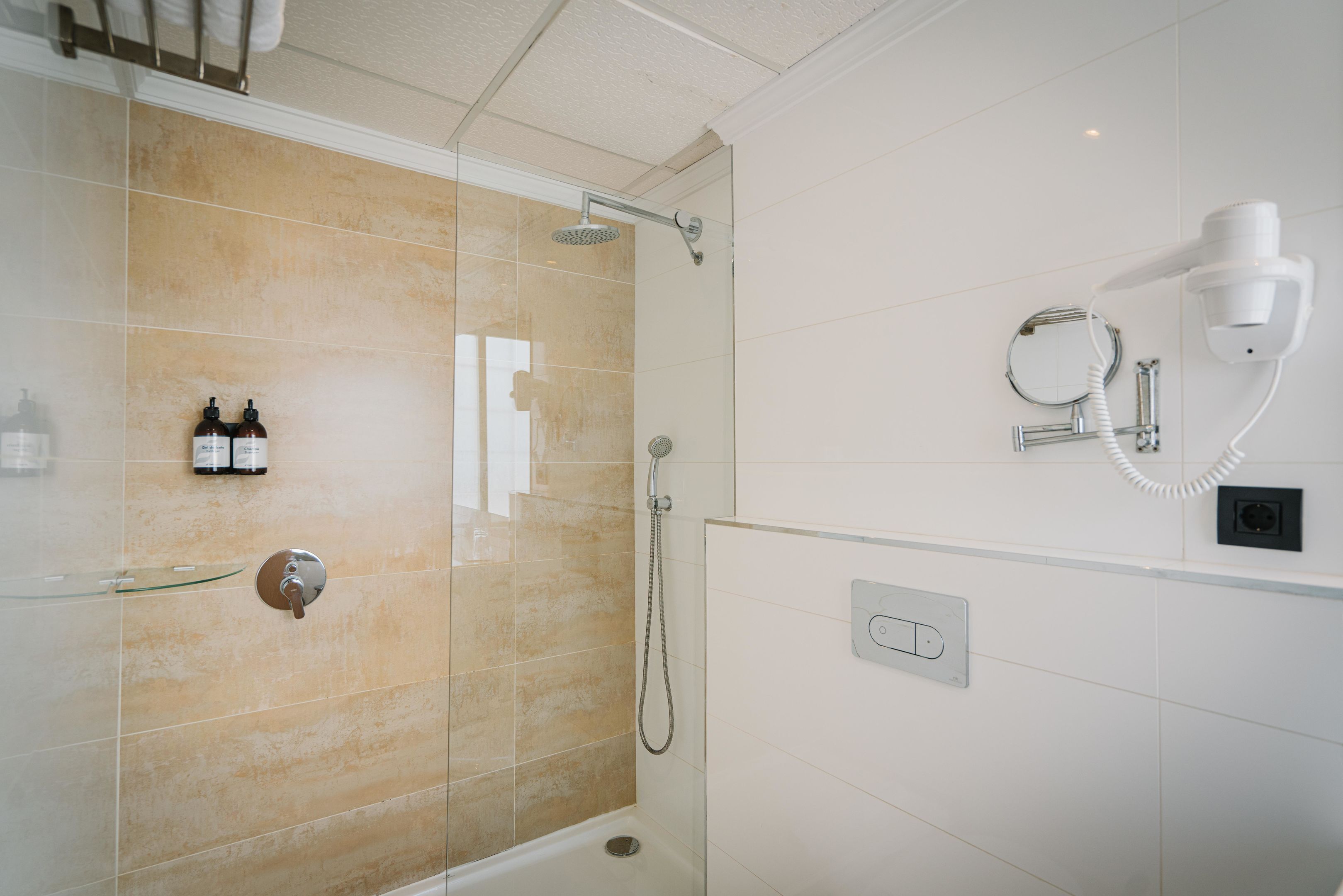 Een moderne badkamer met een douchecabine van glas, een haardroger en een handdoekhouder.