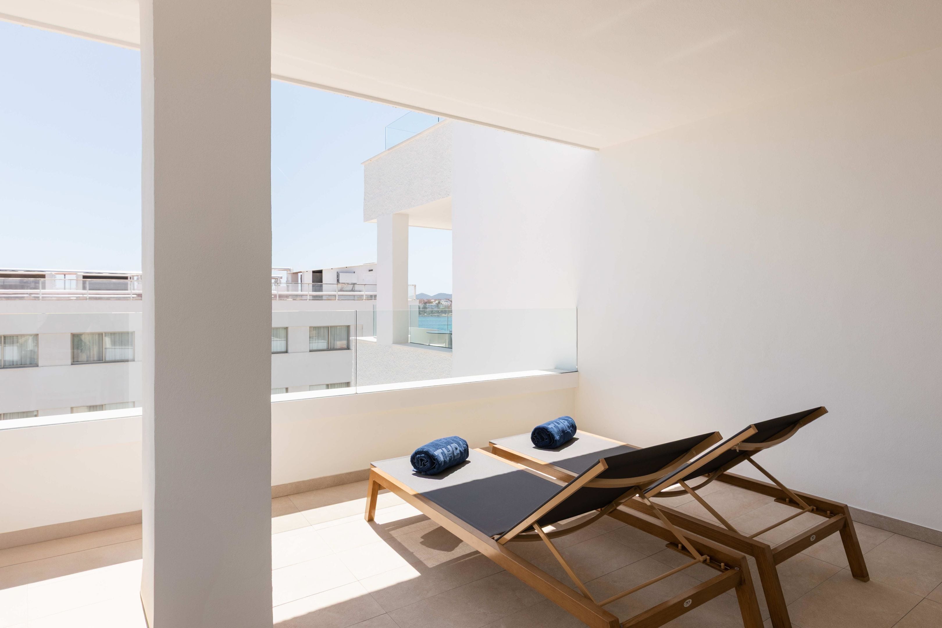 Een balkon met twee loungestoelen, een tafeltje en uitzicht op gebouwen.