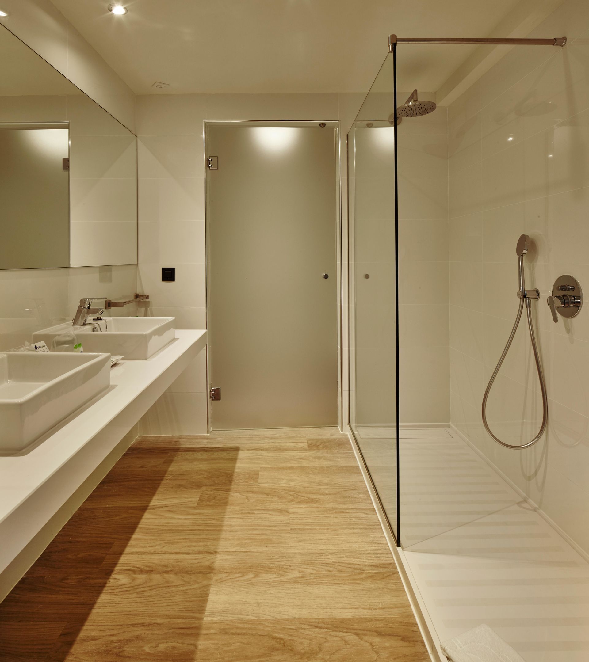 Ein modernes Badezimmer mit einer gläsernen Duschkabine, zwei Waschbecken und Holzboden.