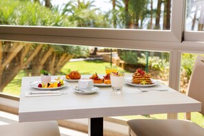 A breakfast table with various dishes and a glass of orange juice, set against a window with a view of greenery. - Hotel THB Los Molinos - Adults Only (Ibiza Town)