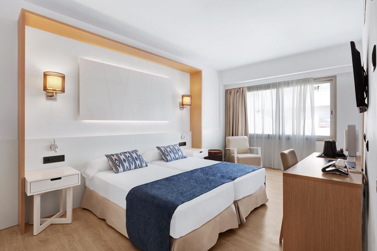 Habitación de hotel con una cama grande, mesitas de noche, un escritorio, una silla y un televisor.
