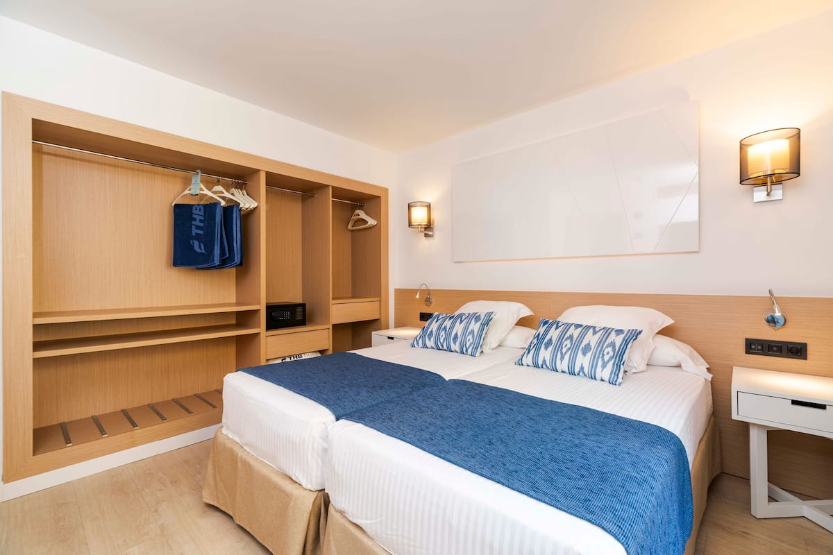 A hotel room with a large bed, a wooden wardrobe, and two bedside tables with lamps.