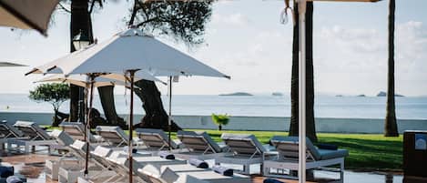 A poolside area with sun loungers and umbrellas, overlooking a body of water.