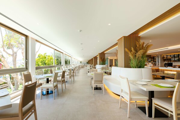 A modern restaurant with long tables and chairs, large windows, and a clean, minimalist interior. - Hotel THB Los Molinos - Adults Only (Ibiza Town)