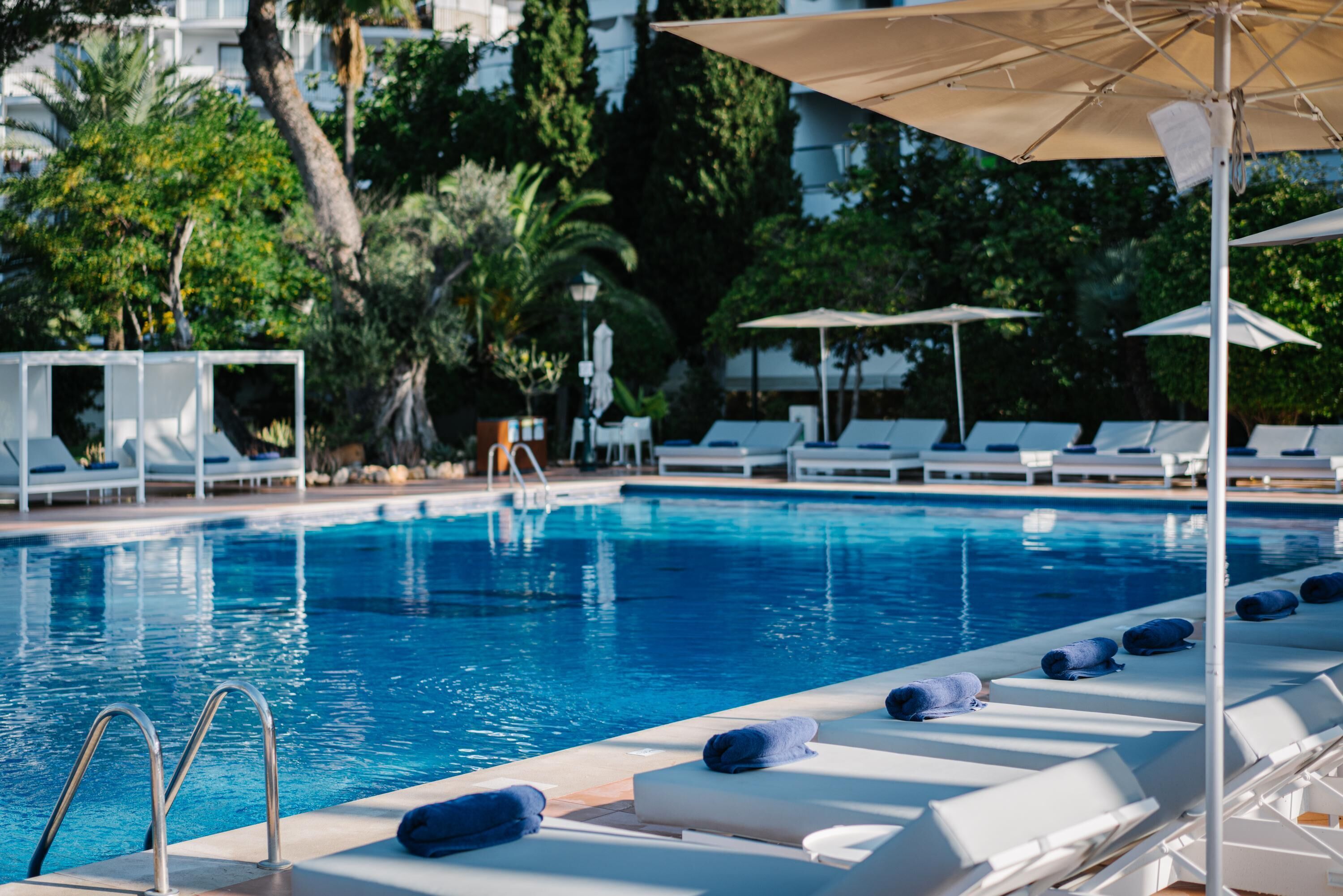 Una piscina con sillones de descanso y sombrillas, rodeada de vegetación.