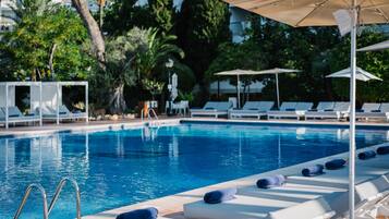 Una piscina con sillones de descanso y sombrillas, rodeada de vegetación.
