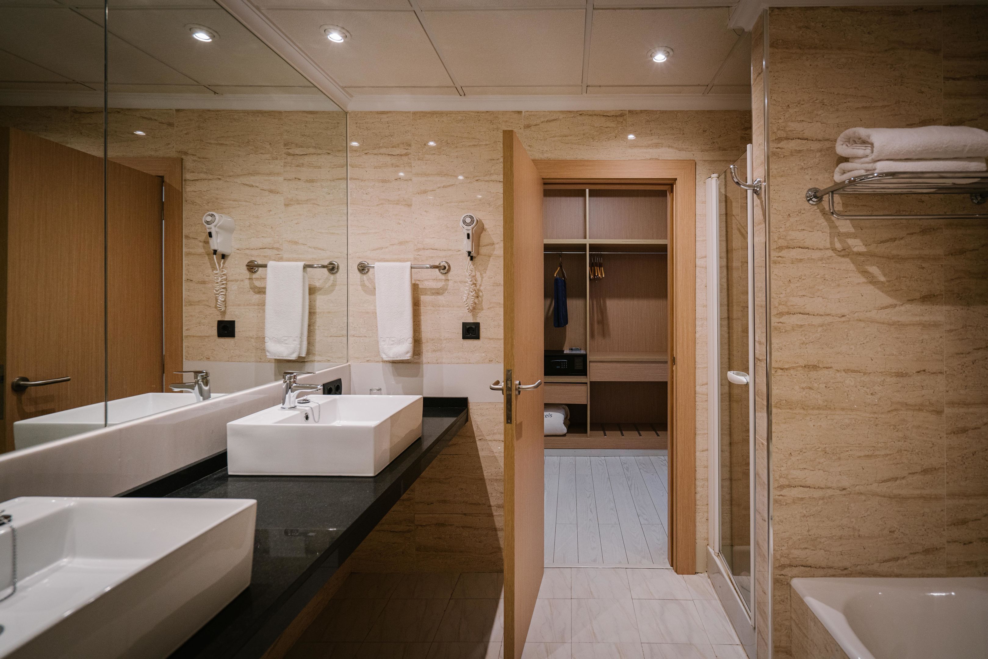 A modern bathroom with two sinks, a shower, and a walk-in closet.