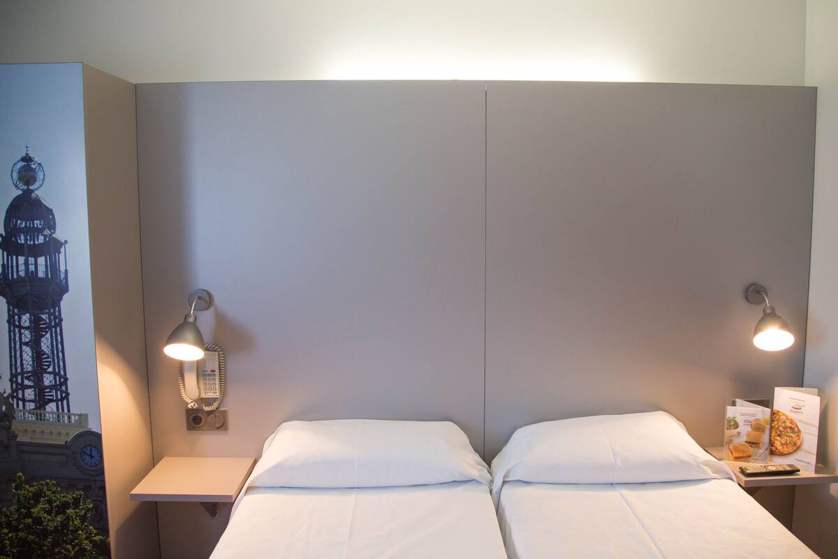 A hotel room with a large bed, two bedside tables, a wall-mounted phone, and two wall-mounted lamps.