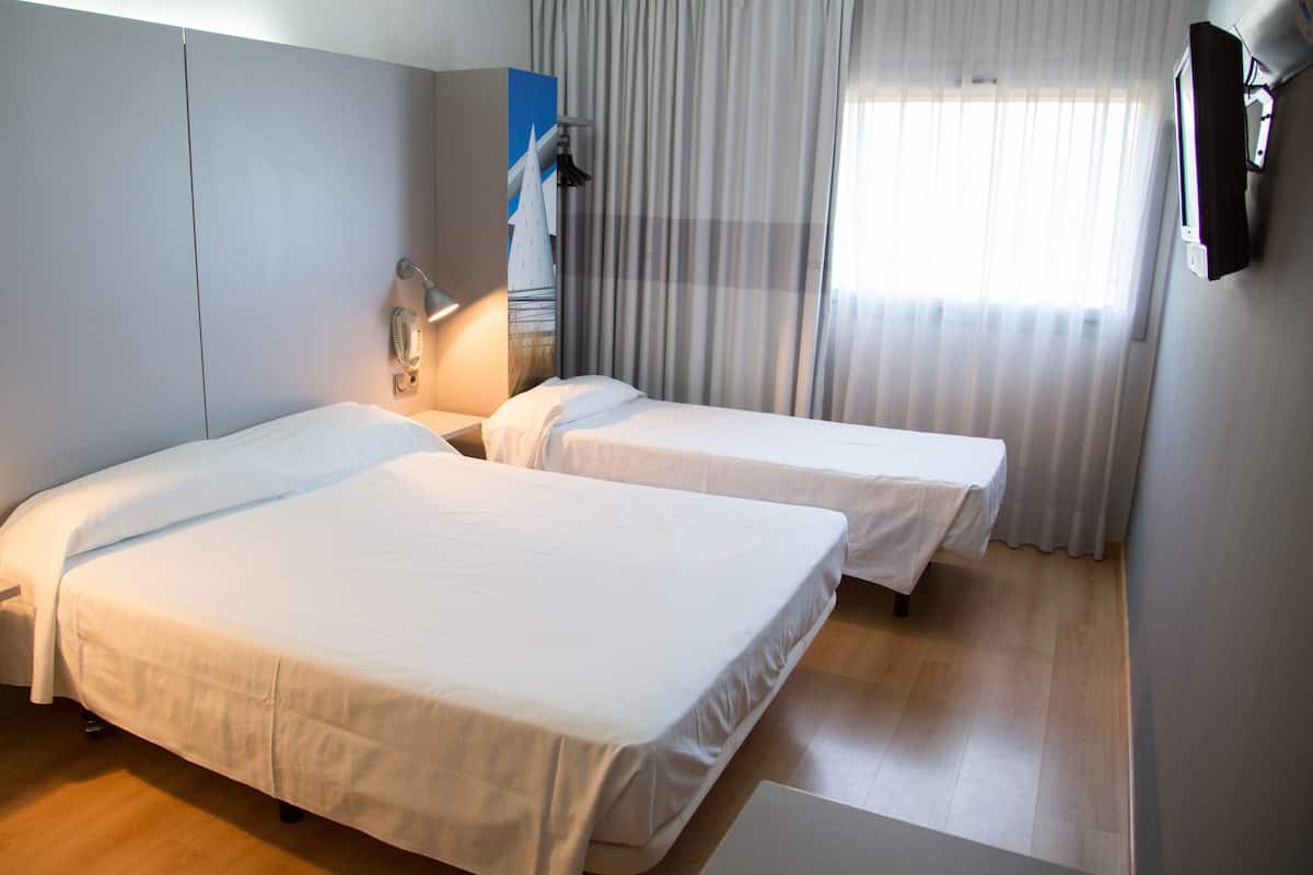 A hotel room with two single beds, a bedside table, a lamp, a painting on the wall, and a window with curtains.