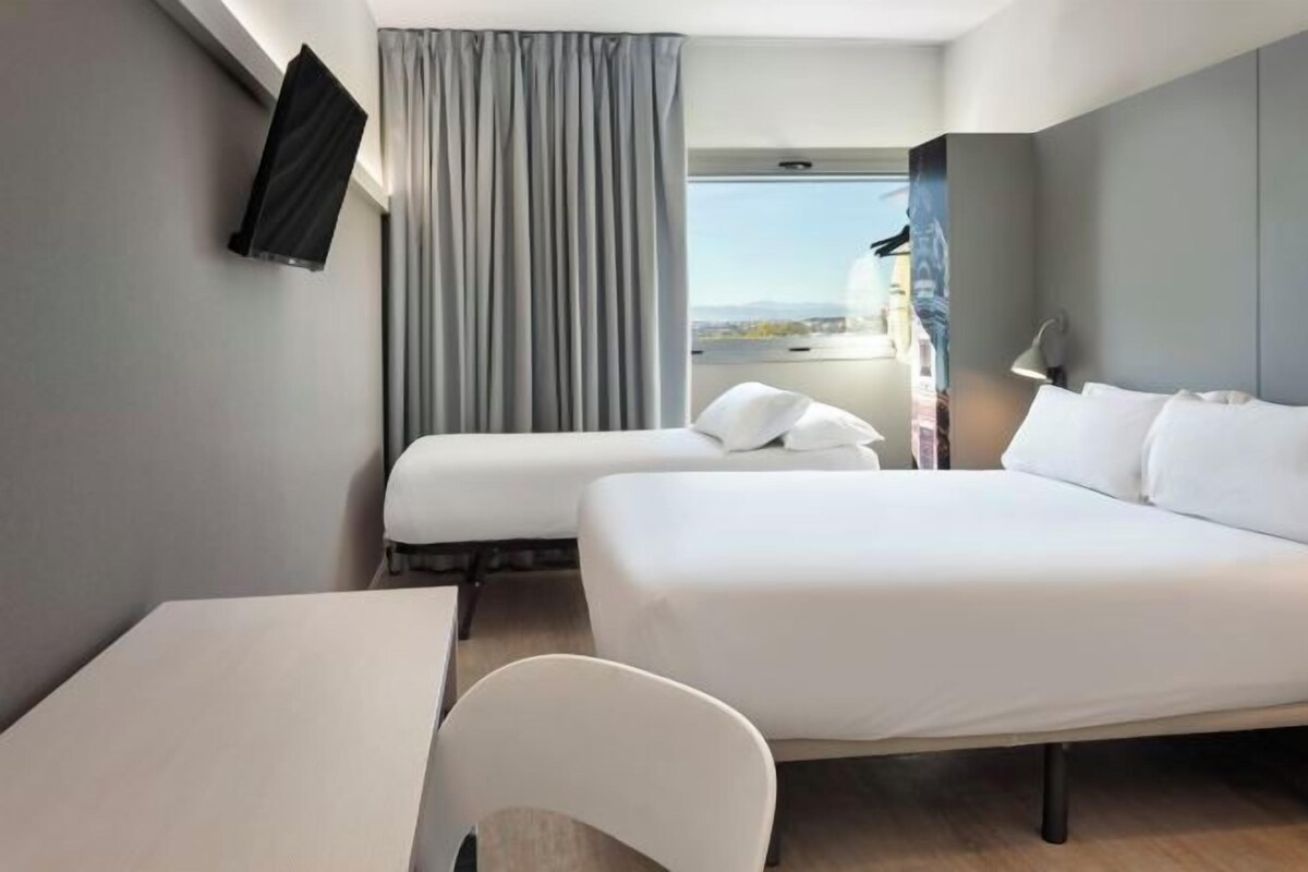 Een moderne hotelkamer met een groot bed, een bureau en een stoel. Er is een raam met uitzicht op de stad.