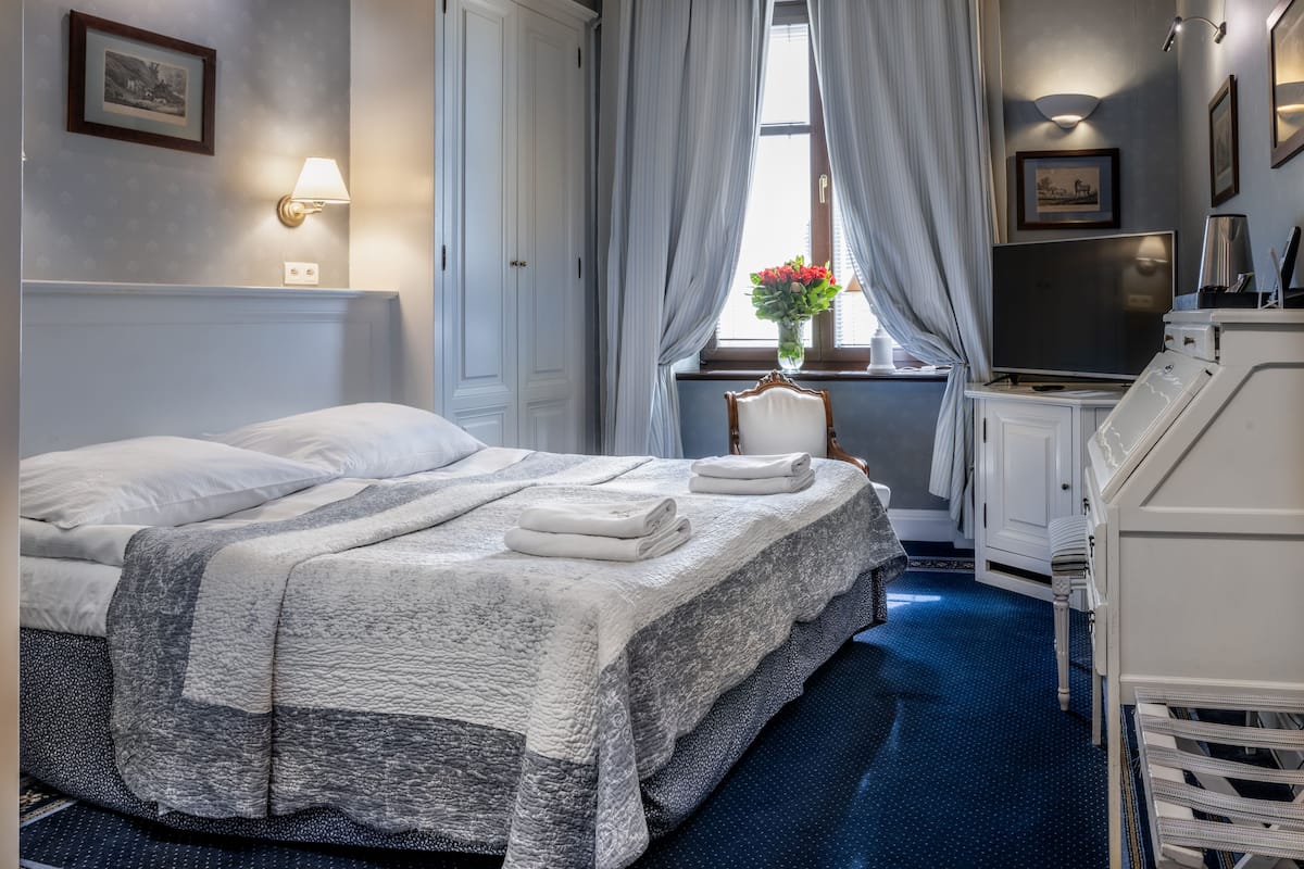 A hotel room with a large bed, a desk, a chair, a TV, and a window with curtains.