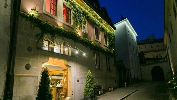 Een hotel met een restaurant op de begane grond, een gevel begroeid met klimop, en een smalle straat.