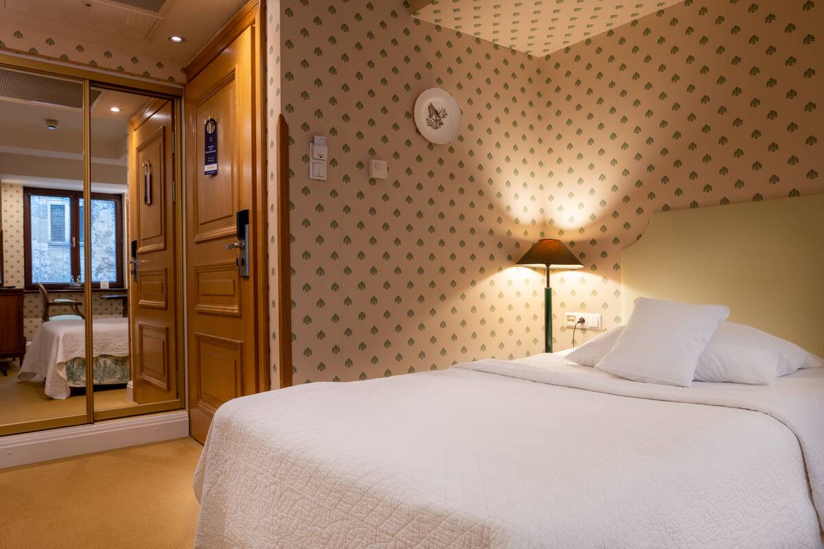 A hotel room with a bed, a wardrobe, and a mirror.