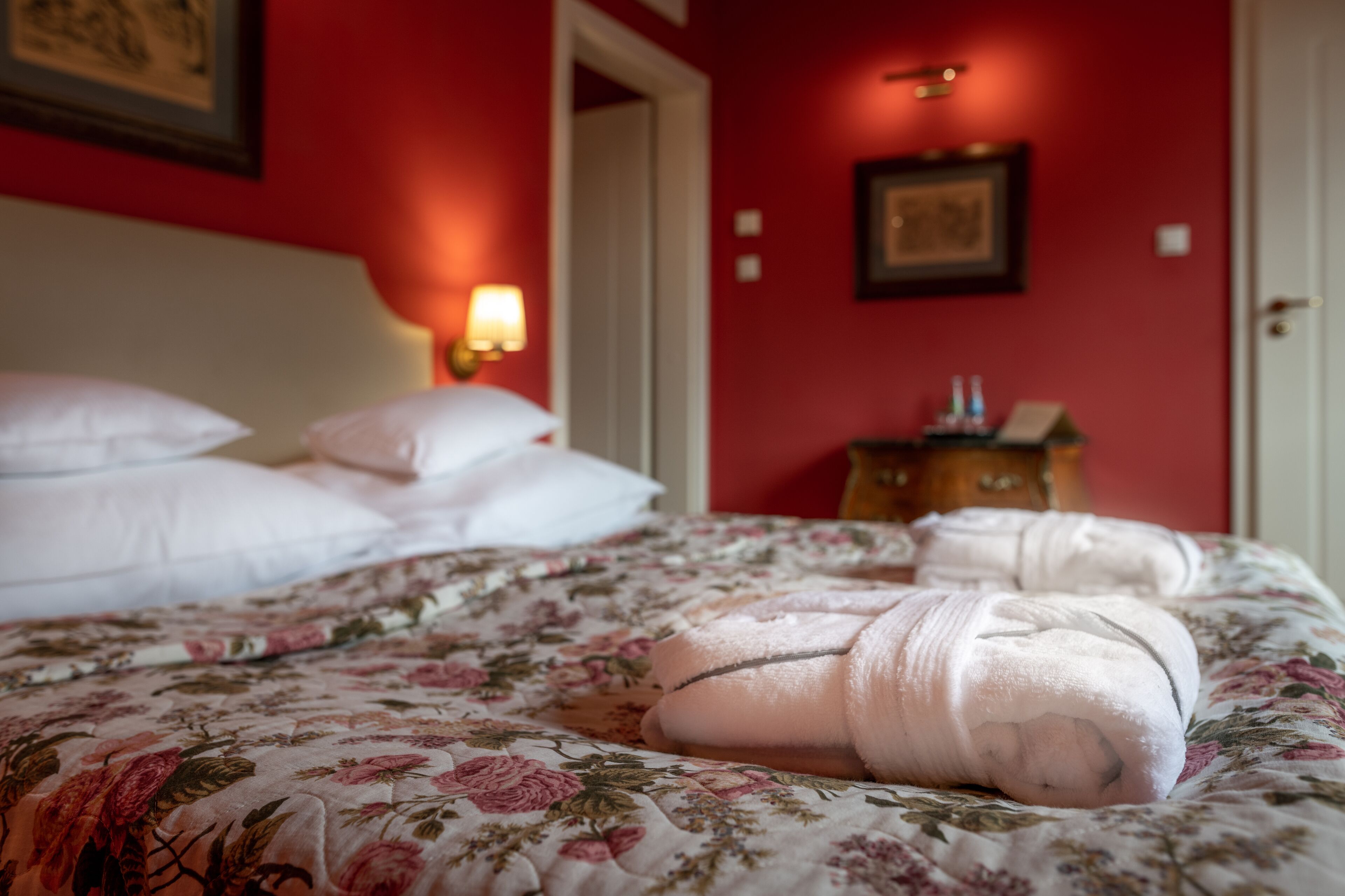 A neatly made bed with floral bedding, a bedside lamp, and a wooden nightstand with a lamp.