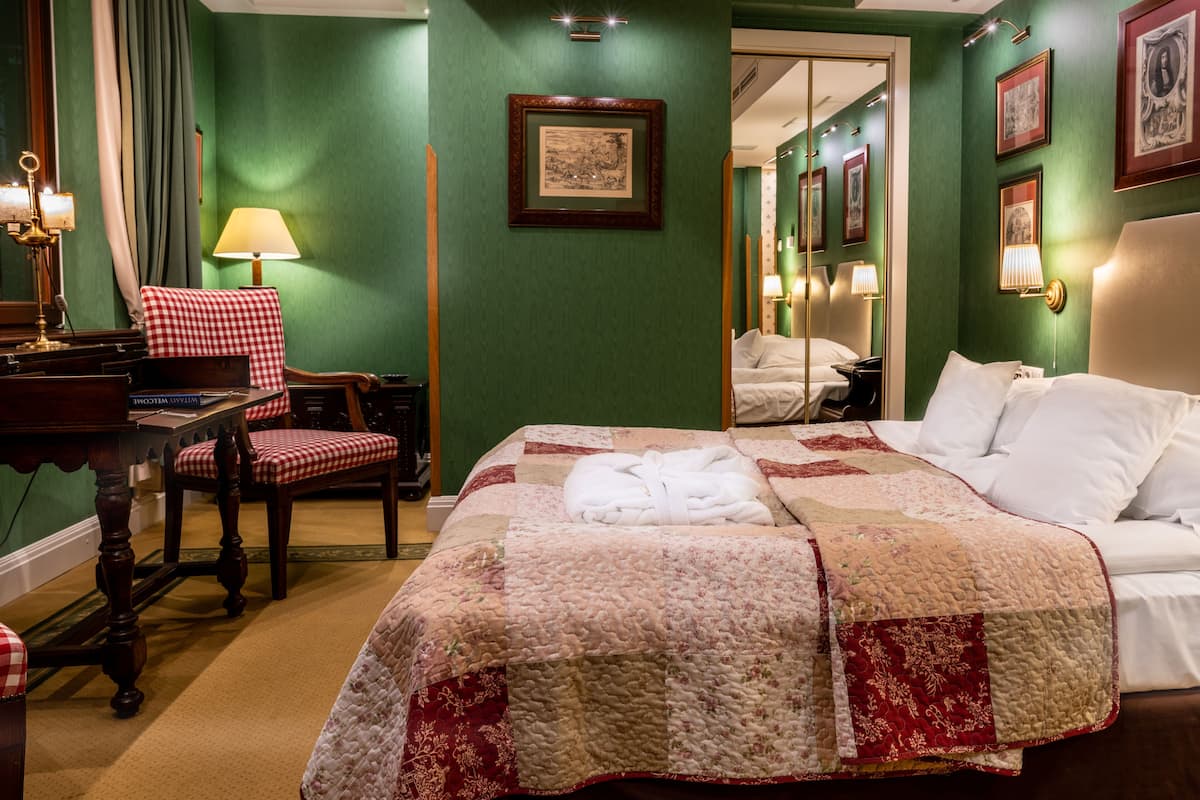 A hotel room with a large bed, a desk with a chair, a lamp, and a mirror.