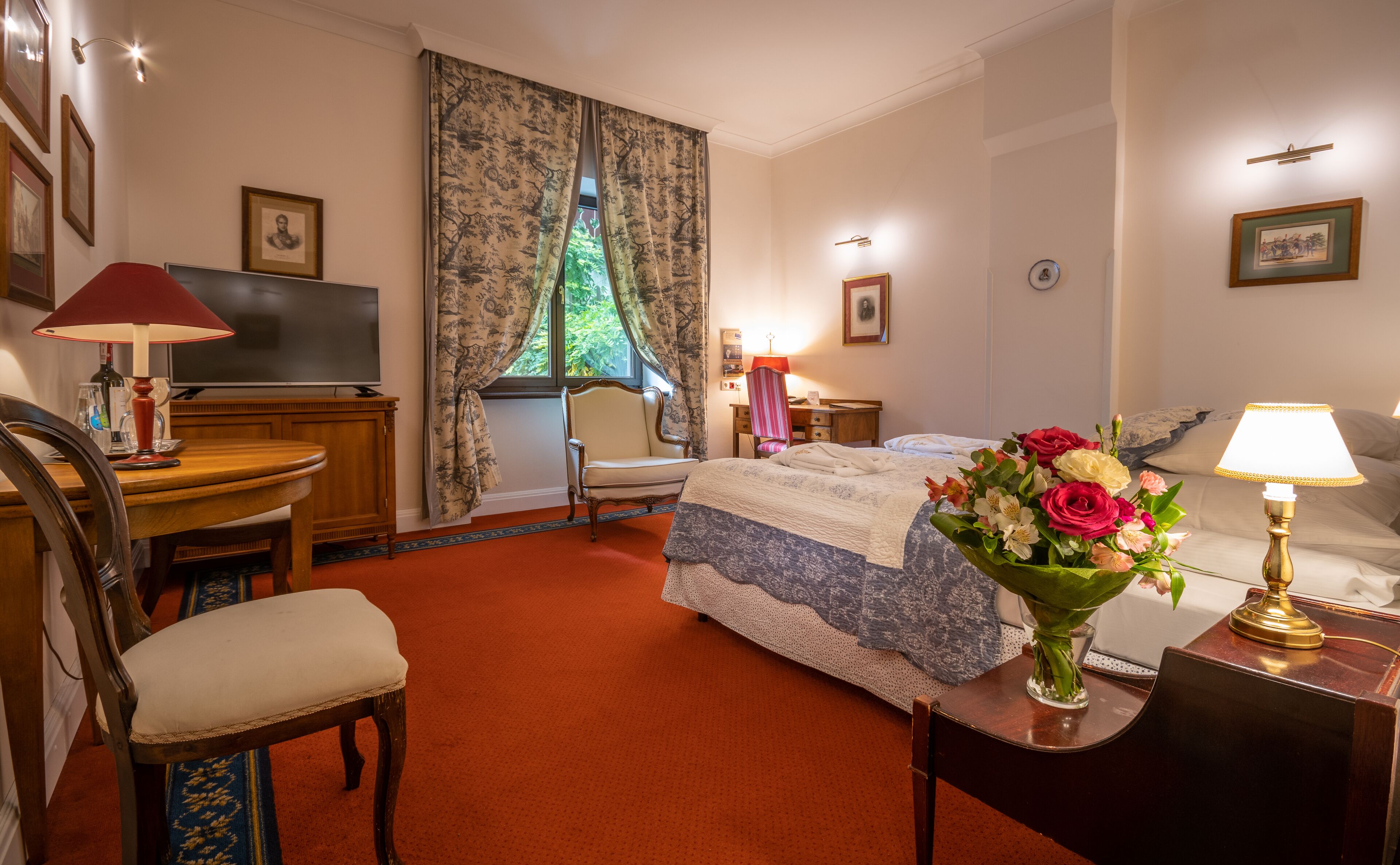 A hotel room with a bed, a desk, a chair, a TV, and a window with curtains.