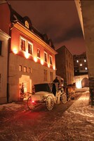 Un carruaje tirado por caballos estacionado frente a un edificio con ventanas iluminadas y un árbol de Navidad.
