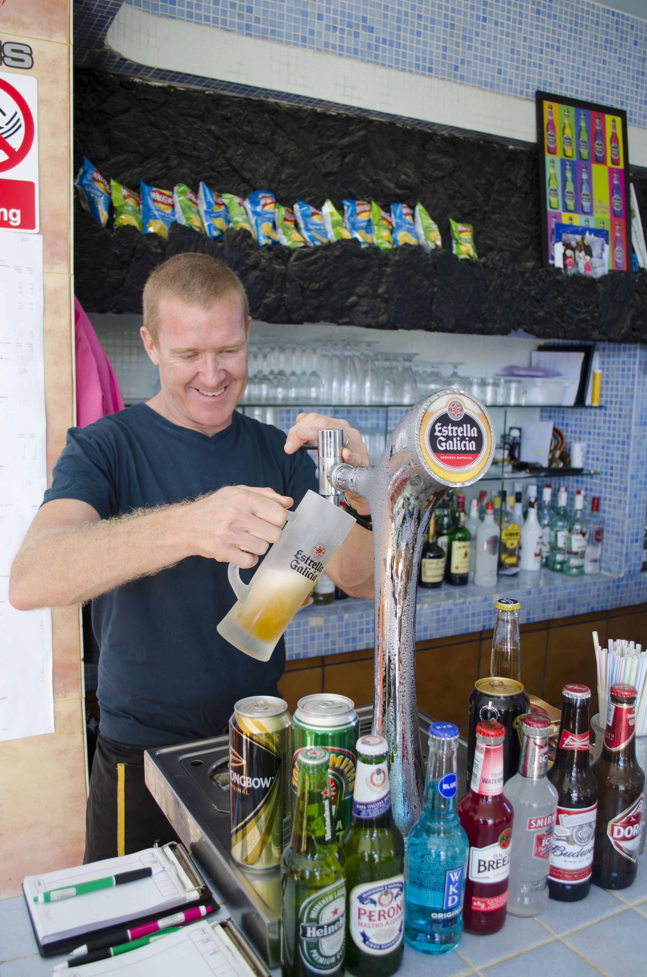 Un camarero sirviendo una bebida de una grifo con la etiqueta "Estrella Galicia" en un vaso.