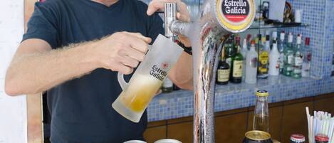 Un camarero sirviendo una bebida de una grifo con la etiqueta "Estrella Galicia" en un vaso.