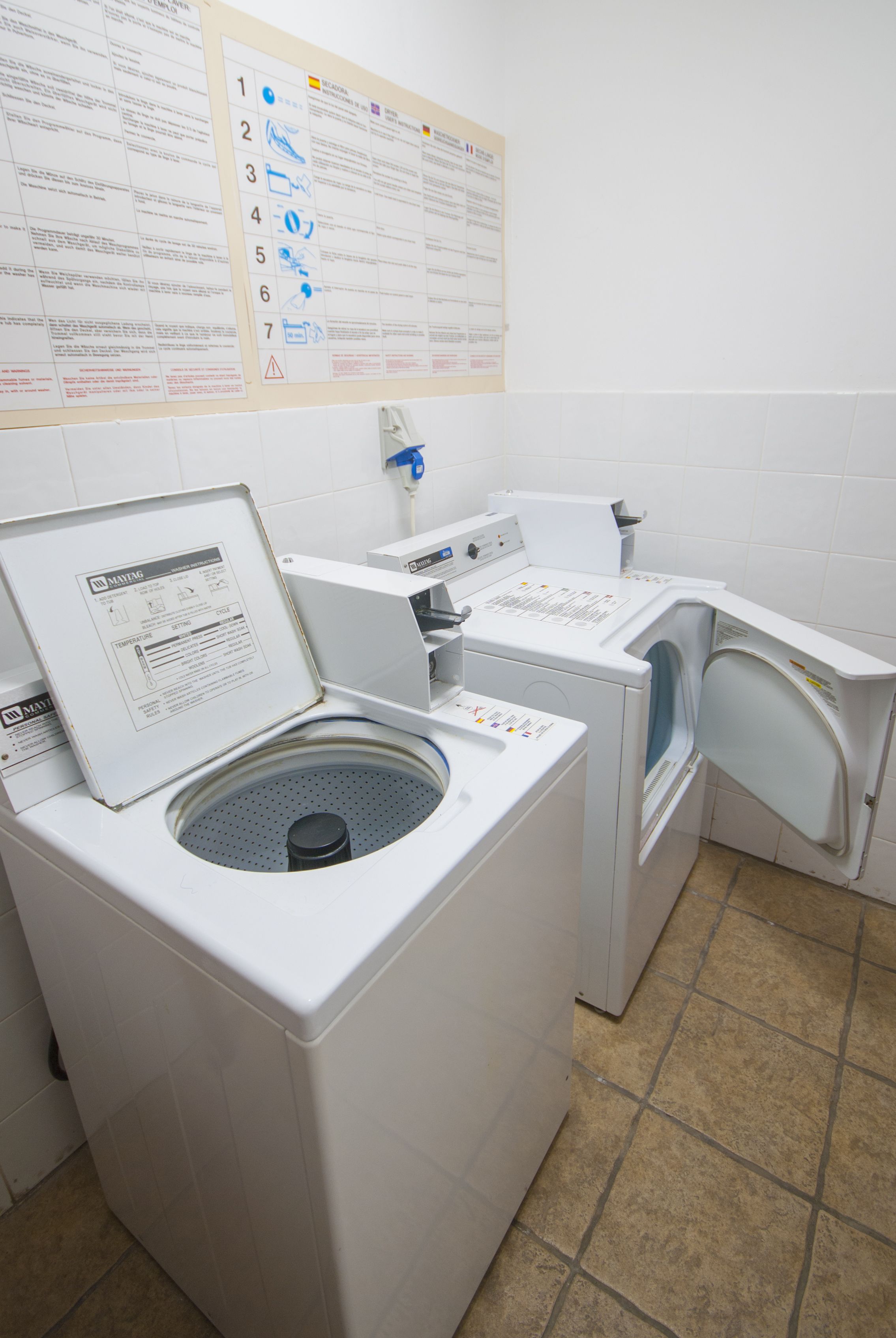Een wasserette met twee wasmachines, een droger en een aan de muur bevestigd instructieboekje.