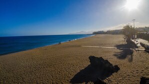 Una extensa playa de arena con cielo azul despejado y el sol brillando intensamente.