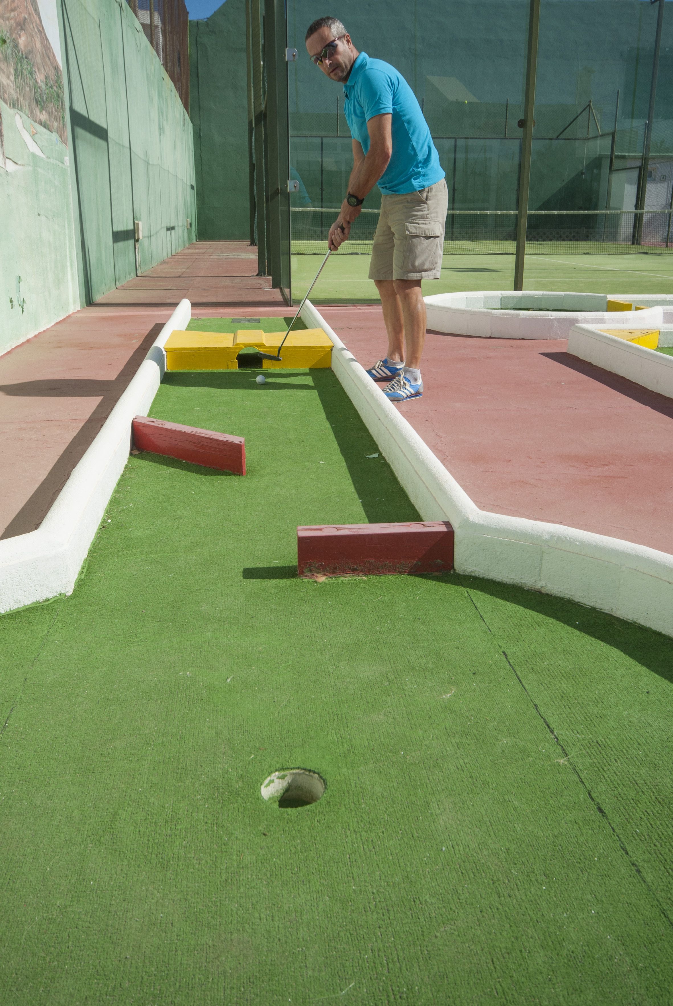 Un homme joue au croquet sur un terrain synthétique vert, délimité par un filet.