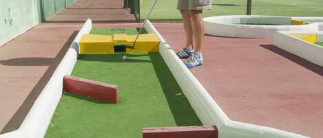 Un hombre juega al croquet en una cancha de césped artificial con una cerca de malla.
