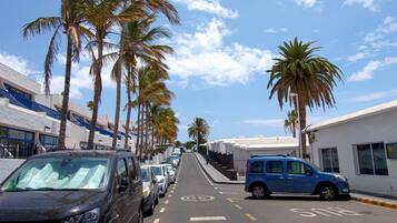 Una calle bordeada de coches aparcados y palmeras, con edificios a ambos lados.