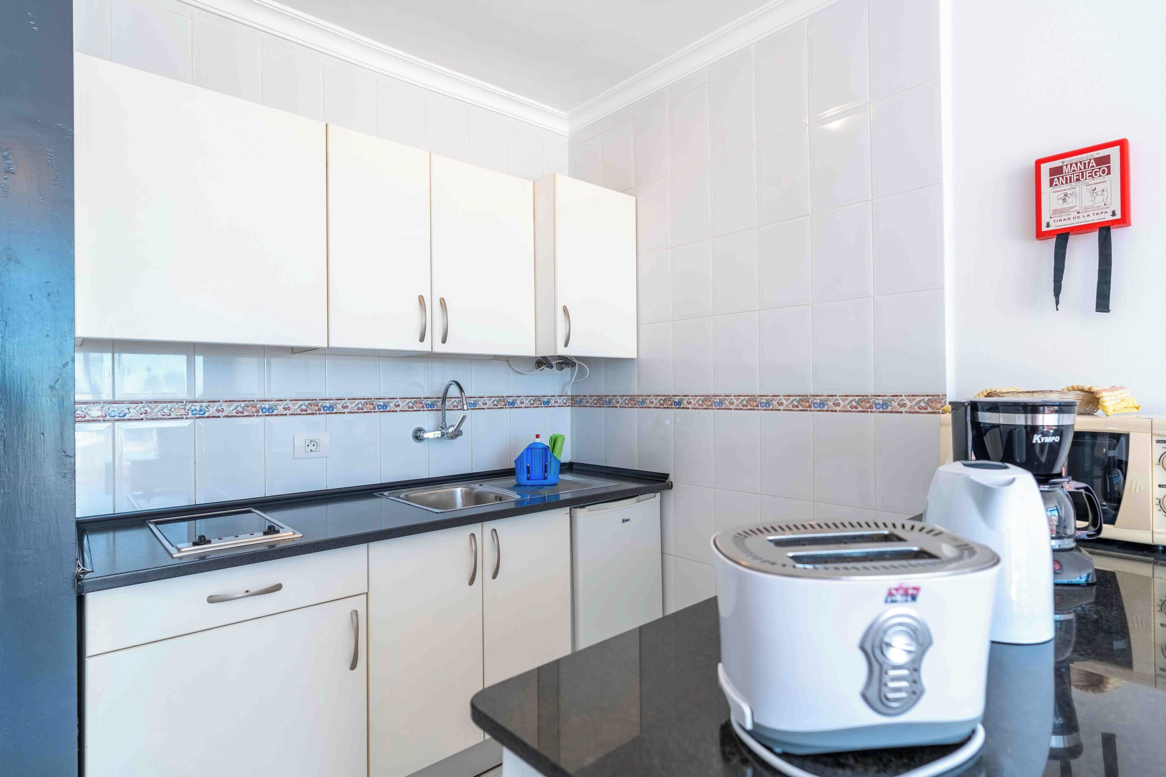 A modern kitchen with white cabinets, a black countertop, a toaster, a coffee maker, and a fire extinguisher.