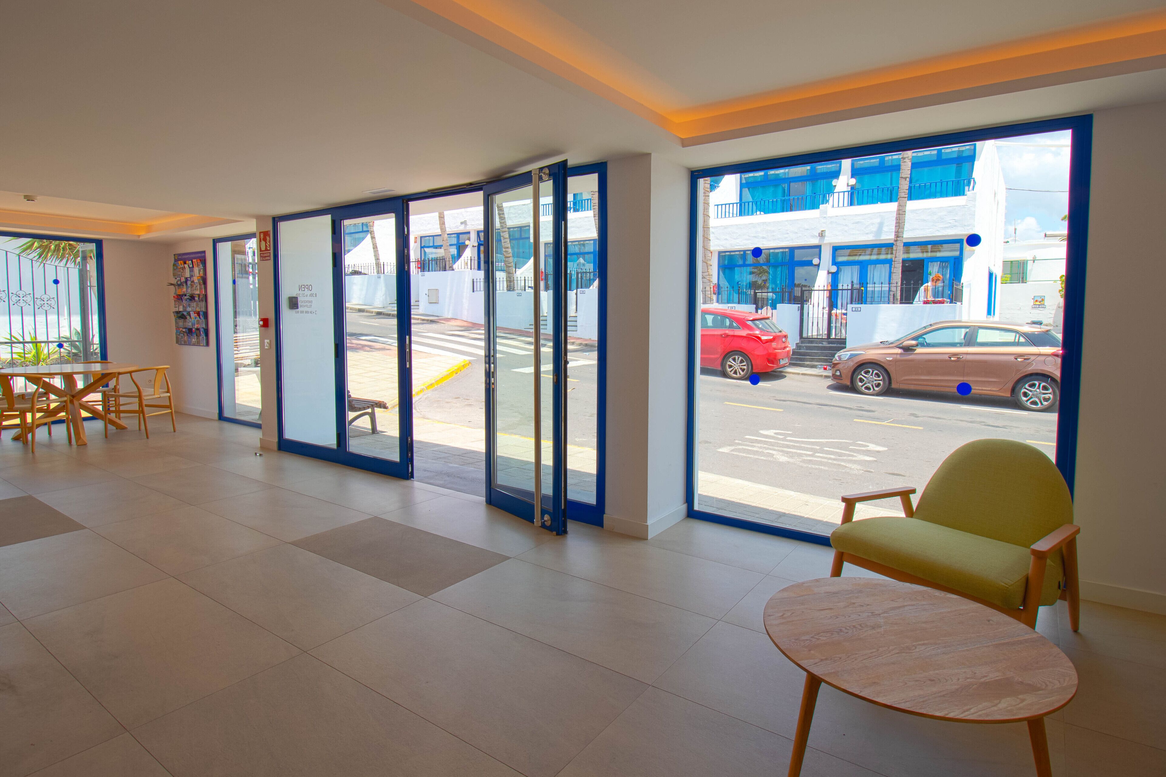 A hotel lobby with a reception desk, seating area, and large windows offering a view of the street.