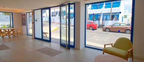 A hotel lobby with a reception desk, seating area, and large windows offering a view of the street.