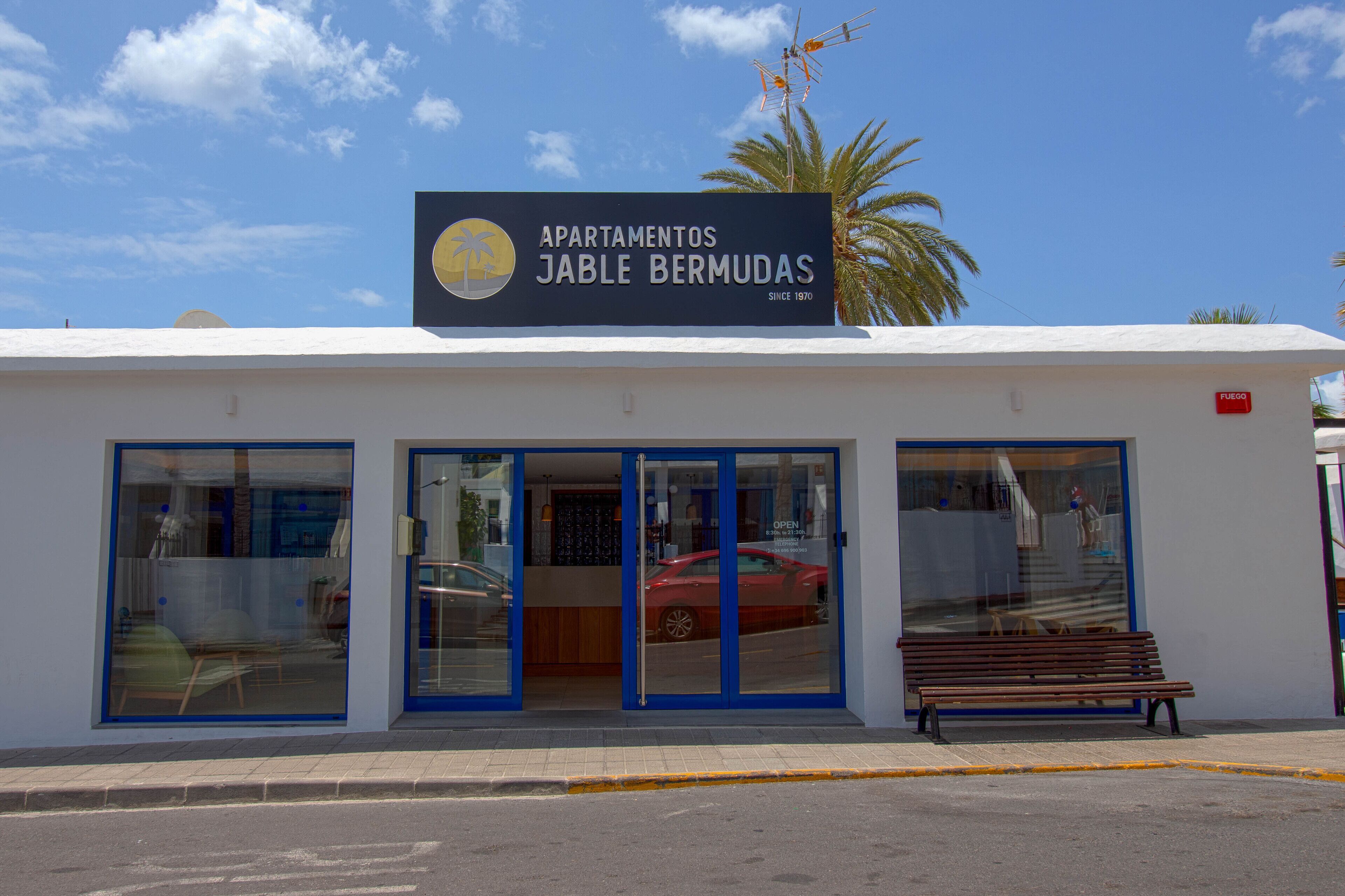 Un edificio con un letrero que dice "Apartamentos Jable Bermudas" y un coche rojo estacionado al frente.
