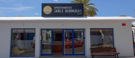 Un edificio con un letrero que dice "Apartamentos Jable Bermudas" y un coche rojo estacionado al frente.