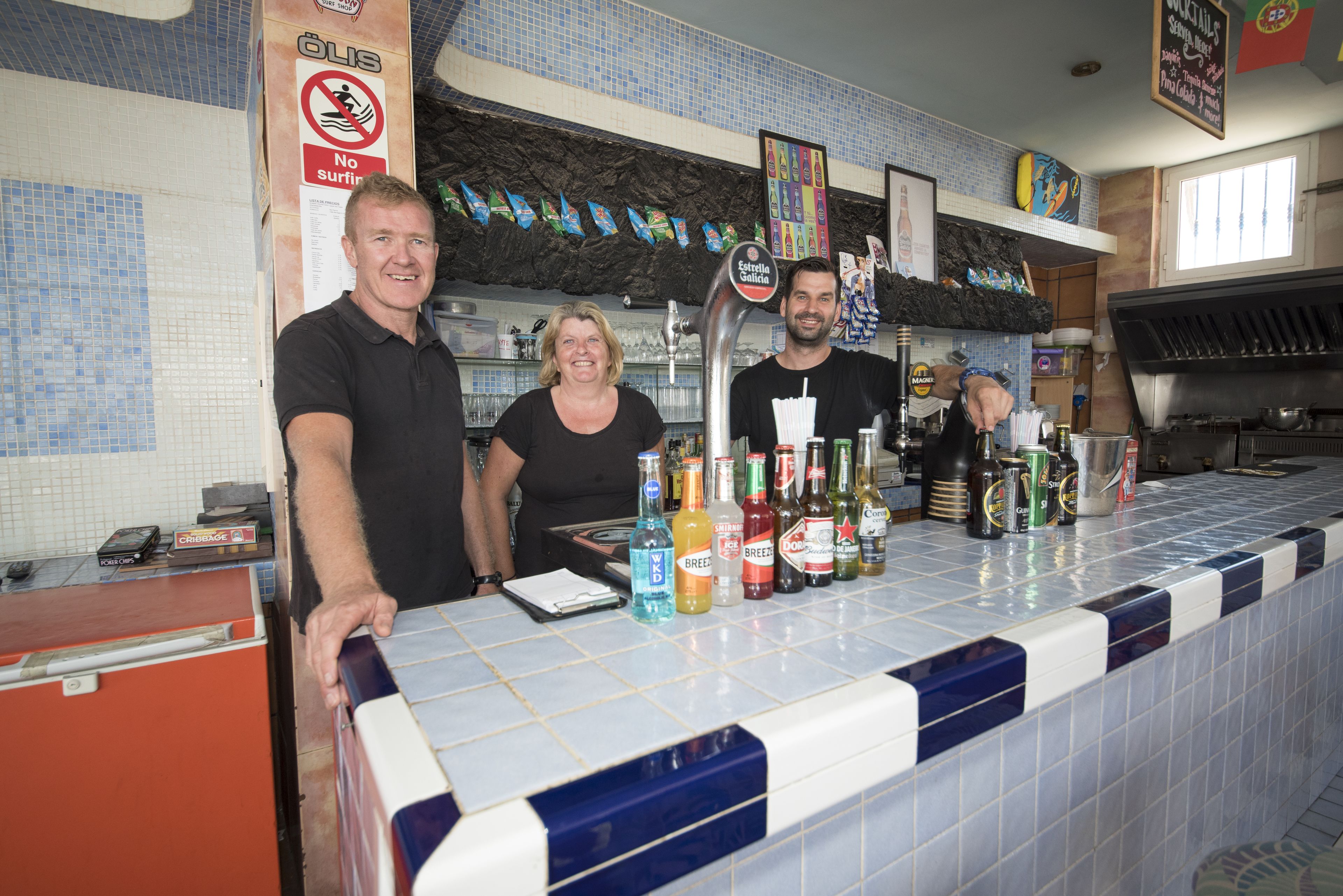 Un bar avec un comptoir carrelé, diverses bouteilles et un panneau indiquant qu’il est interdit d’utiliser un ordinateur portable.