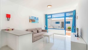 Una sala de estar moderna con un sofá, una mesa de centro, un televisor y un escritorio. Hay un cuadro en la pared y una ventana con cortinas azules.