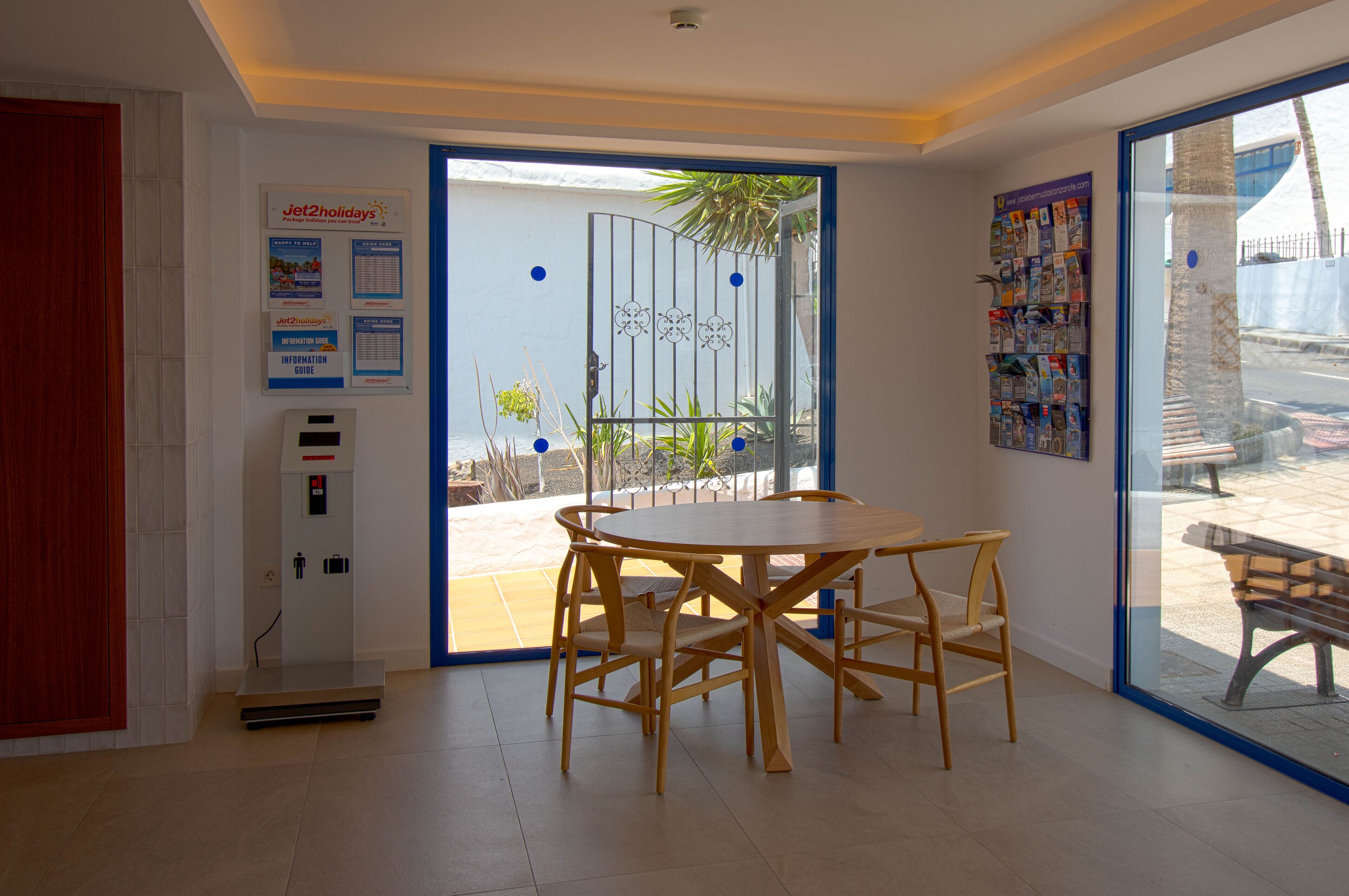 Un interior moderno con una mesa y sillas de madera, una puerta que da al exterior y carteles informativos en la pared.