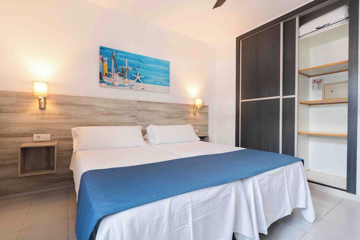 Un dormitorio con una cama, dos luces empotradas en la pared, un cuadro, un armario y una mesita de noche.