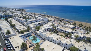 Vista aérea de un complejo turístico frente al mar, con varios edificios, una playa y una piscina.