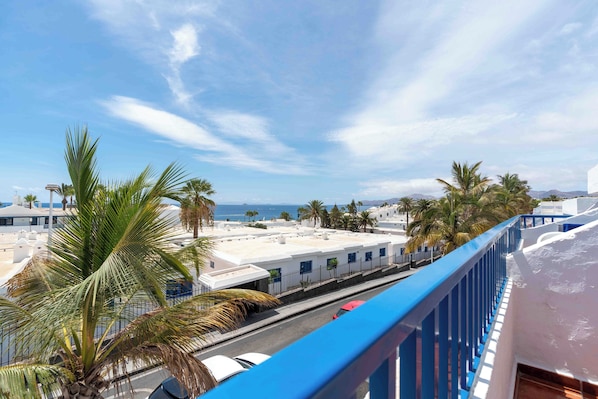 A coastal view with a blue railing, palm trees, and buildings with white facades. - Apartamentos Jable Bermudas (Tías)